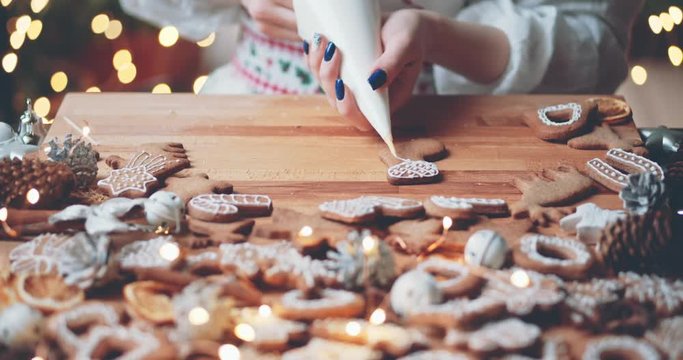 Woman Decorating Baked Gingerbread Christmas Cookies. 4K SLOW MOTION.  Female hands frosting and icing fresh holiday bakery. Festive food, family, Christmas and New Year traditions concept.