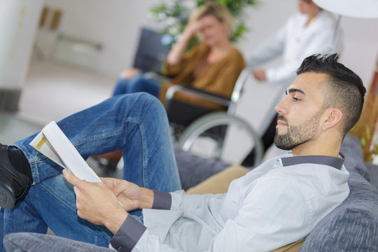 Man In Waiting Room As Patient Gets Pushed Along In Wheelchair