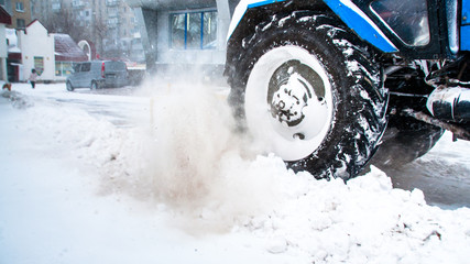 A blue tractor clears snow on the road