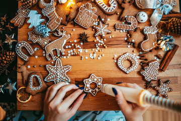 Woman decorating baked gingerbread Christmas cookies with icing and confectionery mastic, view from above. Festive food, family culinary, Christmas and New Year traditions concept.