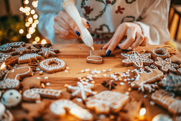 Woman Decorating Baked Gingerbread Christmas Cookies. 4K SLOW MOTION.  Female hands frosting and icing fresh holiday bakery. Festive food, family, Christmas and New Year traditions concept.