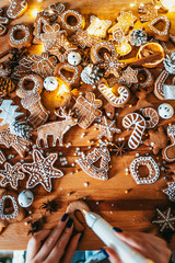 Woman decorating baked gingerbread Christmas cookies with icing and confectionery mastic, view from above. Festive food, family culinary, Christmas and New Year traditions concept.