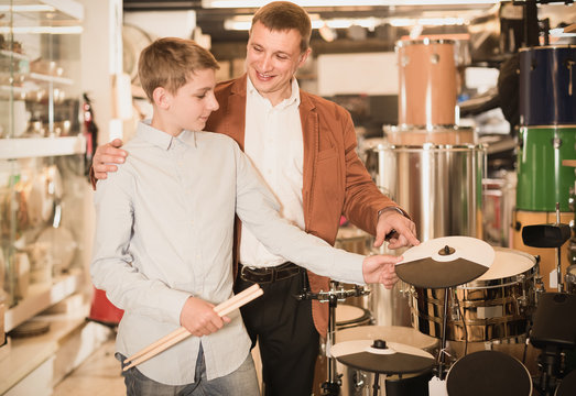 teenager and father deciding on drum unit in musical shop