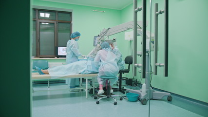 Team of ophtalmology surgeons and assistants with ophtalomological surgery tools during surgical treatment. Through the glass door. Indoor. Wide angle.