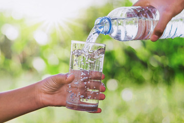 mother's hand pouring drinking water into glass form bottle gives a child © lovelyday12
