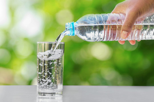 hand pouring drinking water into glass form bottle on table with green blur background