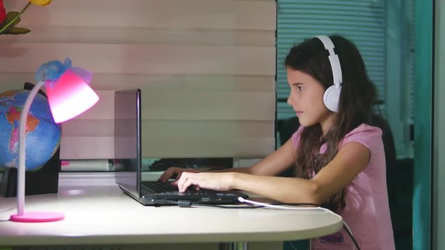 teenage girl with headphones sitting with a laptop. schoolgirl girl playing online game on laptop internet indoors