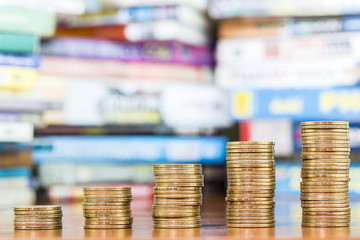 One dollar coins stack arranged as a graph on wood table with blurred pile of book as background, concept of educational advancement and saving money