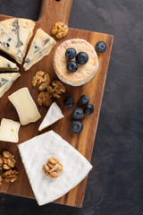 Tasting cheese dish on a dark stone plate. Food for wine and romantic date, cheese delicatessen on a black concrete background. Top view