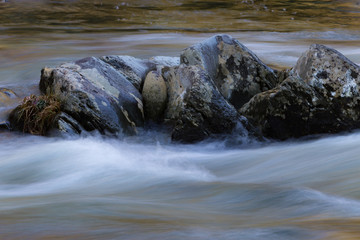 Lichen covered rock formation surrounded by swiftly running waters, horizontal aspect