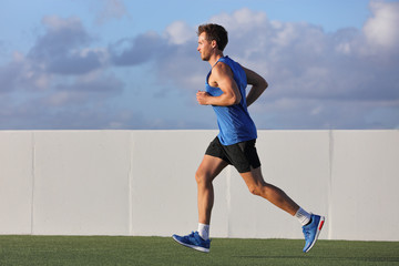Young man runner running in city park on summer grass outdoors at sunset at outdoor stadium fitness...