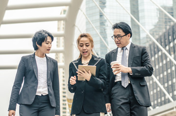 young businessmen and two lady in classic suits are holding cups of coffee, talking and smiling, standing outside the office building.