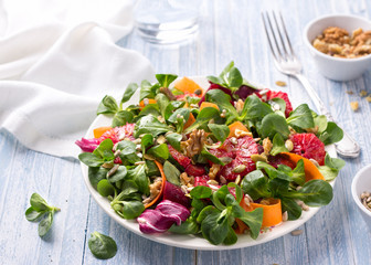 Green salad with blood oranges, carrots, beets, seeds and nuts on a light blue background, free space. Delicious healthy food