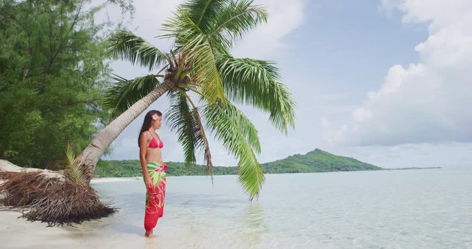 French Polynesia Vacation Travel woman relaxing on paradise beach on holidays on Matira Beach, Bora Bora. Happy girl on beach vacation wearing traditional pareo and Bikini in Tahiti, French Polynesia.
