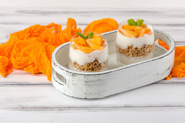 Persimmon creamy trifle in beautiful glasses, fresh ripe fruit slices on white wooden background. Healthy vegetarian food. Delicious dessert. Close up photography. Selective focus.
