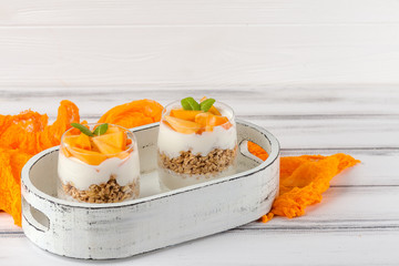 Persimmon creamy trifle in beautiful glasses, fresh ripe fruit slices on white wooden background. Healthy vegetarian food. Delicious dessert. Close up photography. Selective focus.
