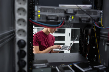 Portrait of modern young man holding laptop standing in server room working with supercomputer