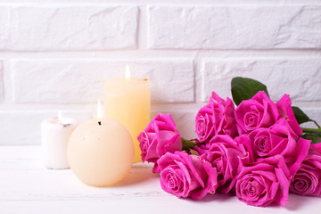 Obraz na płótnie Canvas Bunch of pink roses flowers and three burning candles on white wooden background
