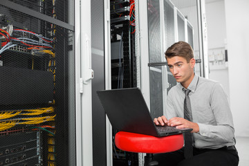 Portrait of modern young man holding laptop standing in server room working with supercomputer