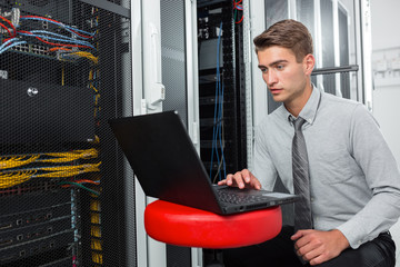 Portrait of modern young man holding laptop standing in server room working with supercomputer