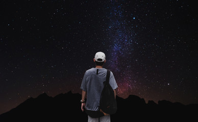 Fototapeta premium a man with backpack standing alone with colorful stars on night sky background