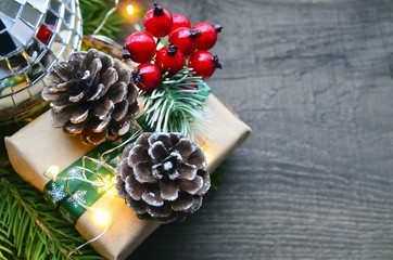 Christmas decoration with fir tree,gift box,red berries,garland lights and pine cones on old wooden background.Winter holidays,Merry Christmas,Happy New Year concept. Copy space.Selective focus.