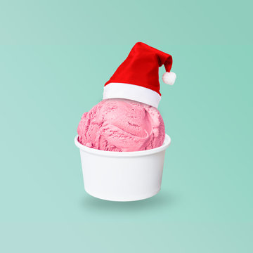 Santa Claus red hat on real strawberry ice cream scoop in paper cup isolated on green background (Clipping path included) to celebrate Christmas holiday season, new year party or special event