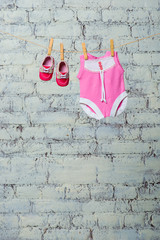 Children's pink body, bib and red shoes, dry on a rope against a white brick wall.