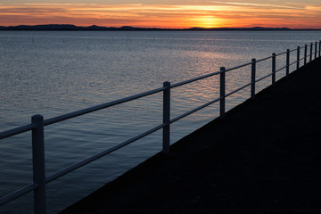 Obraz premium A pier silhouette on a lake at sunset, with beautiful soft and warm colors in the sky and water