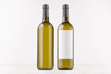 Two green wine bottles with blank white label and without label, on white wooden board, mock up. Template for advertising, design, branding identity.