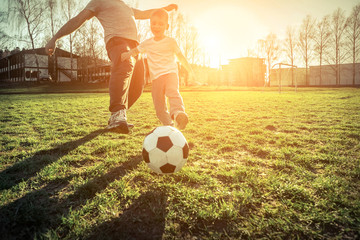 Father and son playing together with ball in football under sun