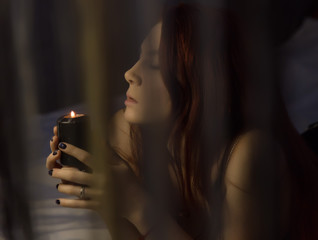 sensual redhead woman lies on a bed and holding black burning candle