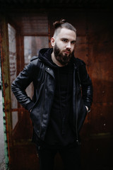 Obraz premium Modern young bearded man in black style clothes standing in urban background.