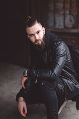 Fototapeta na wymiar Modern young bearded man in black style clothes standing in urban background.