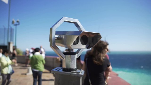 Binoculars at observation deck on sunny day, people moving around at background