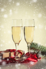 The concept of Christmas. Two glasses with champagne, a gift and a fur-tree branch. Snowfall