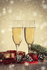 Сoncept of Christmas and New Year. Two glasses with champagne, a gift and fir cones. Snowfall