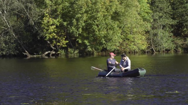 Two fisherman in rubber boat floats rowing with oars on river. Man is fishing on lake in sunny forest. Stracha river - beautiful place close to Belarusian nuclear power plant