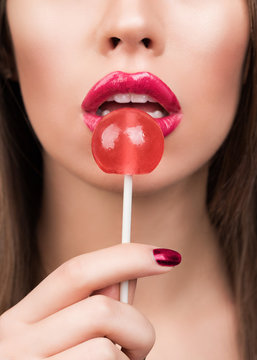 Beauty fashion model with colourful lollipops. Young pretty woman with makeup, pink lips and long hair holding sweet red candy.