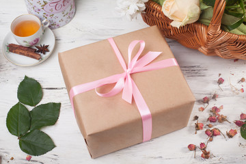 Gift box in kraft paper with satin ribbon on a wooden table flowers