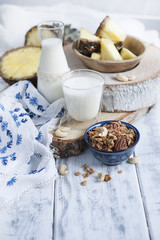 Milk in a glass and in a bottle, muesli in a blue cup. on a white wooden background and pineapple and tablecloth with blue flowers