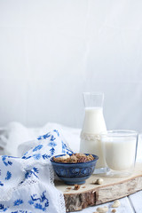 Milk in a glass and in a bottle, muesli in a blue cup. on white wooden background and tablecloth...
