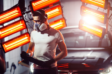 man wearing protective mask and glasses holding polishing machine with red warm lights in background