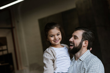 cheerful father and daughter hugging and looking at camera at home