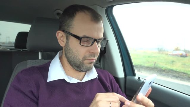 Businessman using a smartphone while sitting inside car. Man with a smart-phone in the  vehicle.