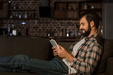 smiling man sitting on couch and using tablet at home