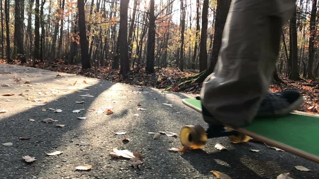 Man skating longboard towards the camera on the leafs covered path.