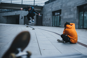man sitting on floor and taking photo of skateboarder doing trick