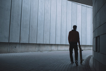 skateboarder standing with board in front of grey concrete wall