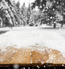 Wooden desk covered by snow and snowy park on background